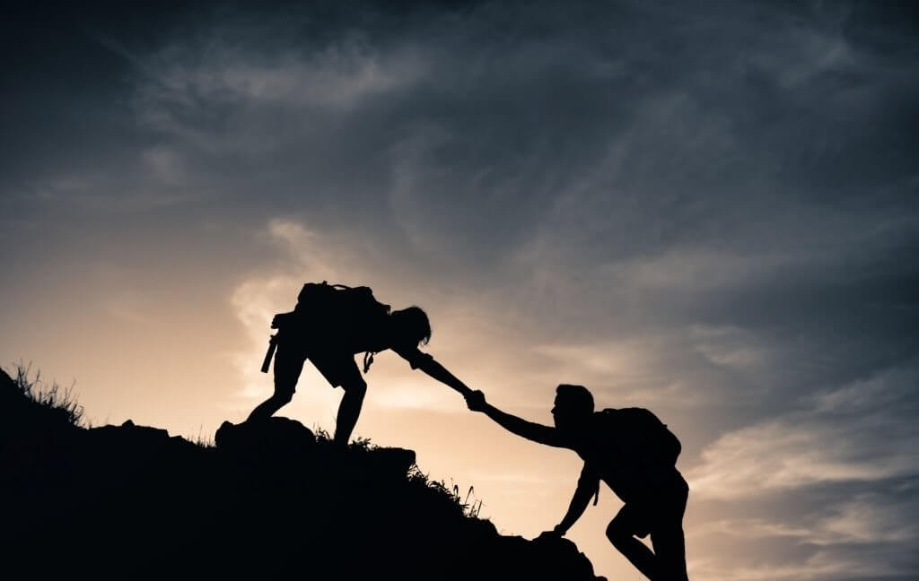 Persona en la cima de una montaña ayudando a otra